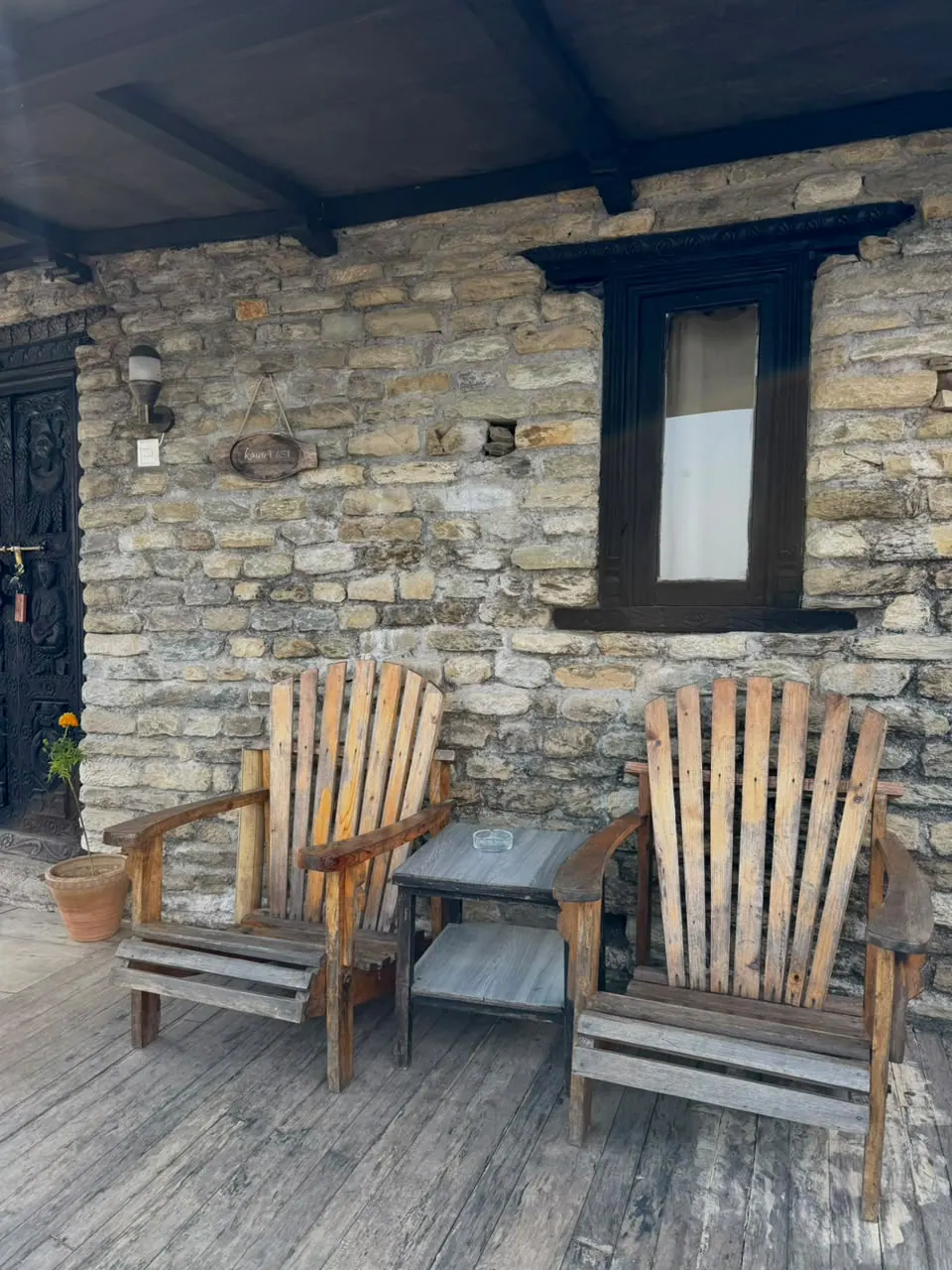 Two wooden armchairs on Kausi East's terrace against a stone wall with a carved wooden window